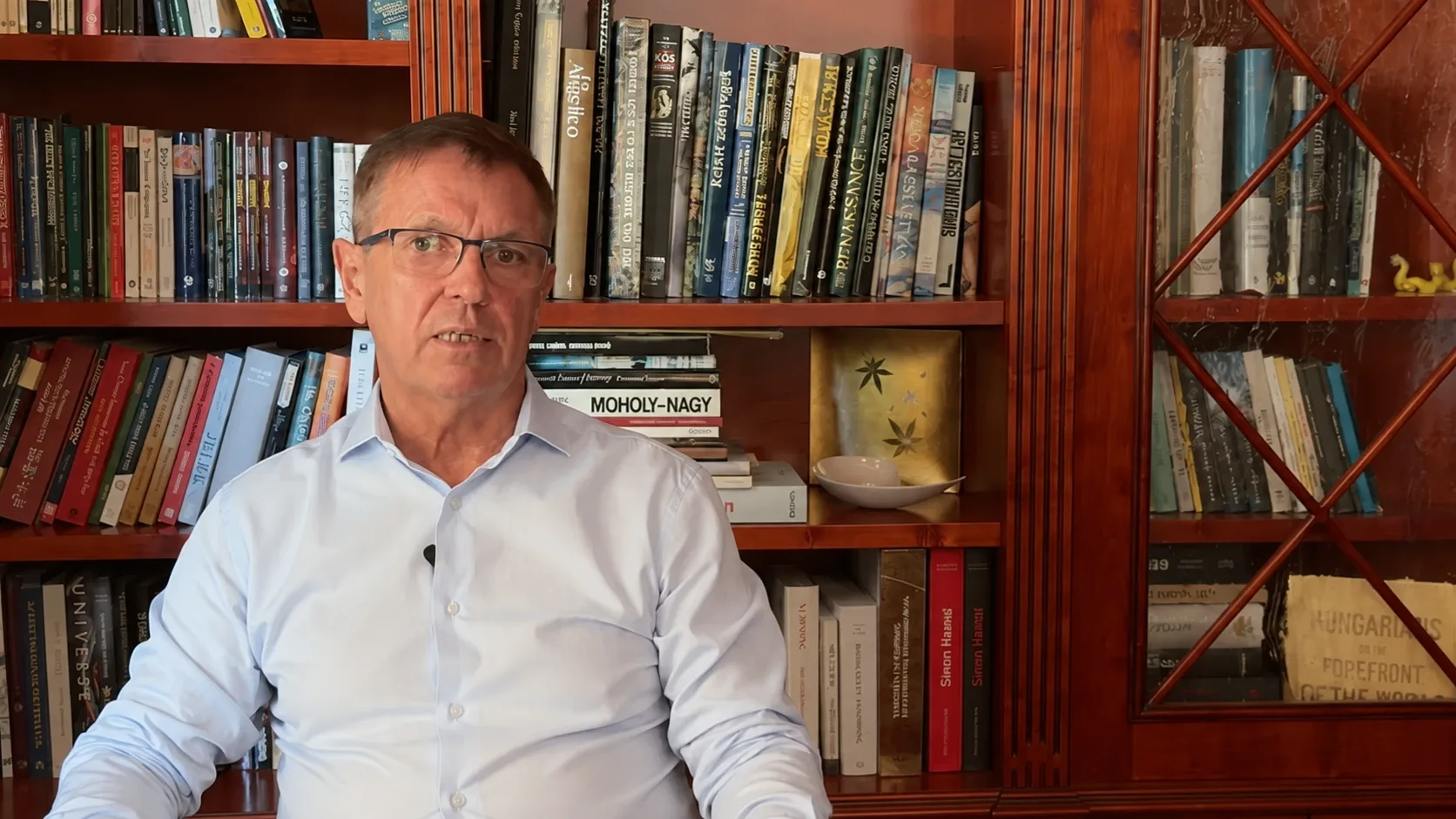 Matolcsy György volt jegybankelnök egy könyvespolc előtt ülve beszél egy videófelvételen