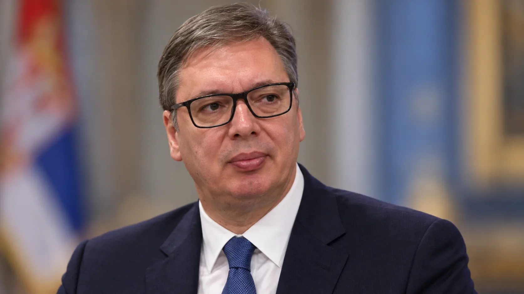 Aleksandar Vučićot ábrázoló AI-generált portré sötét öltönyben, kék nyakkendővel és fekete keretes szemüvegben.