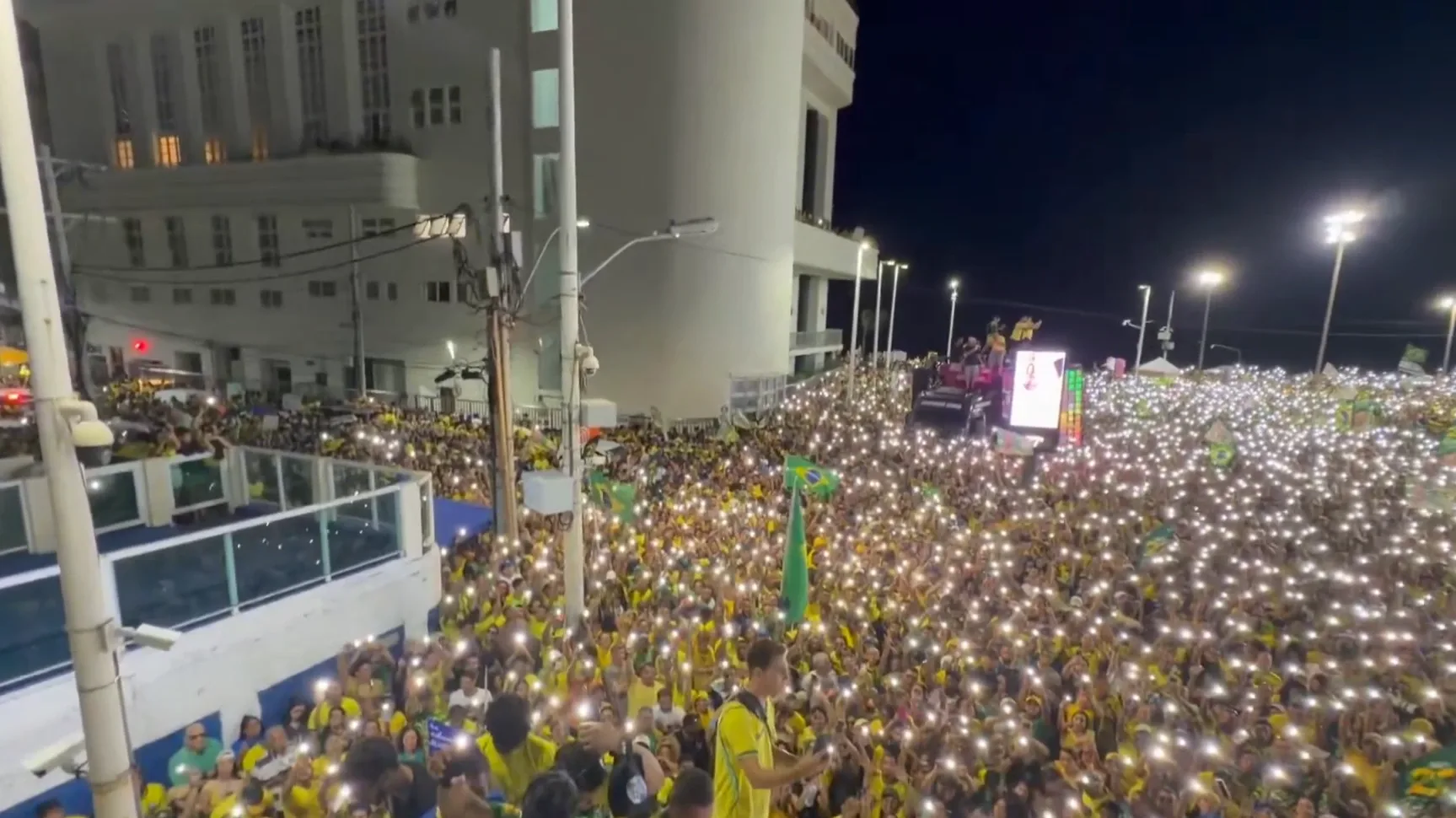 Hatalmas tömeg brazil zászlókkal és világító mobiltelefonokkal egy éjszakai politikai rendezvényen Brazíliában.