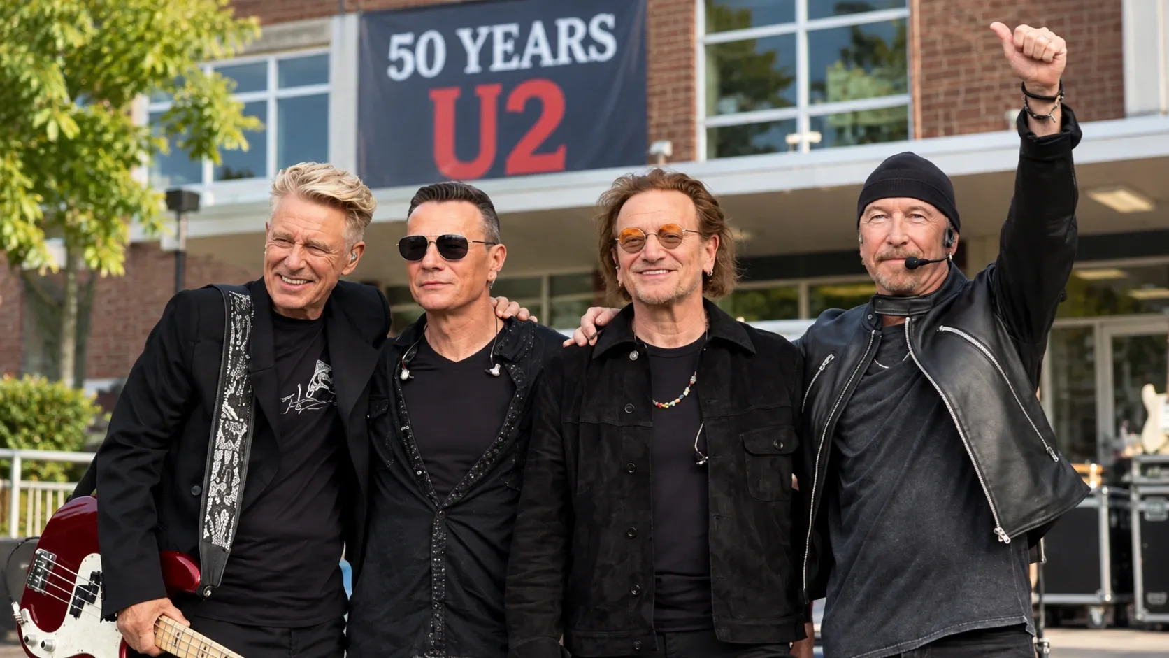 A U2 négy tagja egy dublini iskola előtt az együttes ötvenedik évfordulóján – illusztráció.