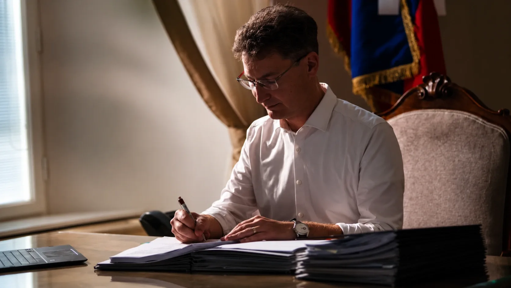 Cser-Palkovics András dokumentumokat ír alá az íróasztalánál.