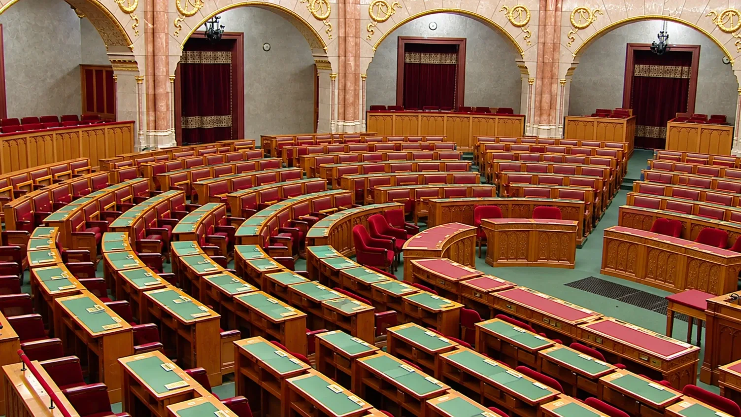 Üres parlamenti ülésterem vörös székekkel, fa padsorokkal és díszes belső térrel.