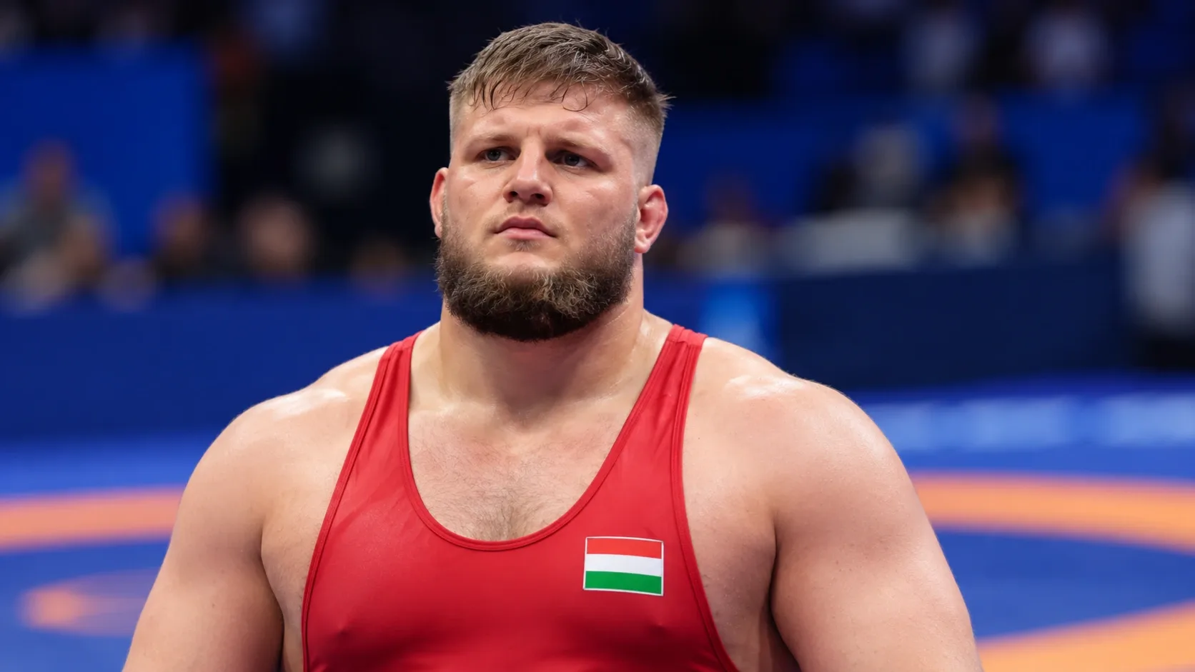 Vitek Dáriust ábrázoló AI-generált portré piros birkózómezben, elmosódott sportcsarnoki háttérrel.