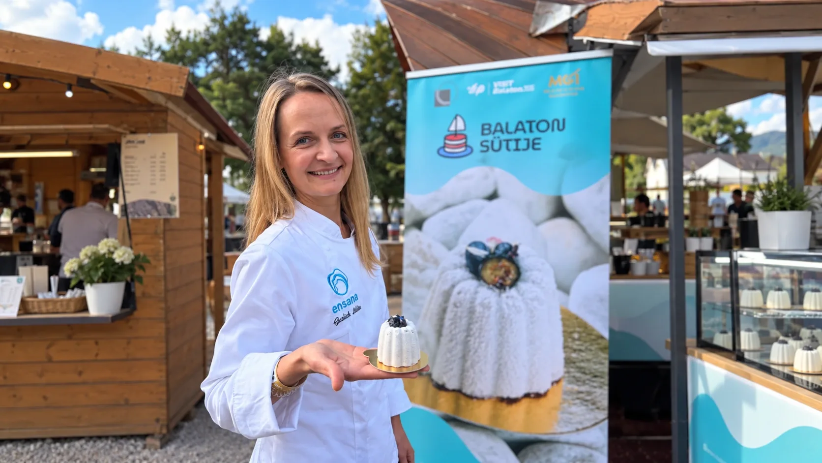 Gevlich Liliia fehér cukrászkabátban mutatja a Kék Balaton desszertet, a verseny molinója előtt.