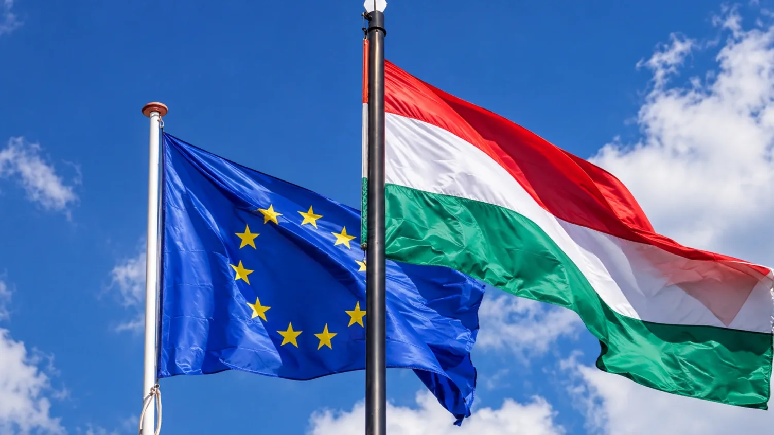 Magyar és európai uniós zászlók lobognak a kék ég előtt.