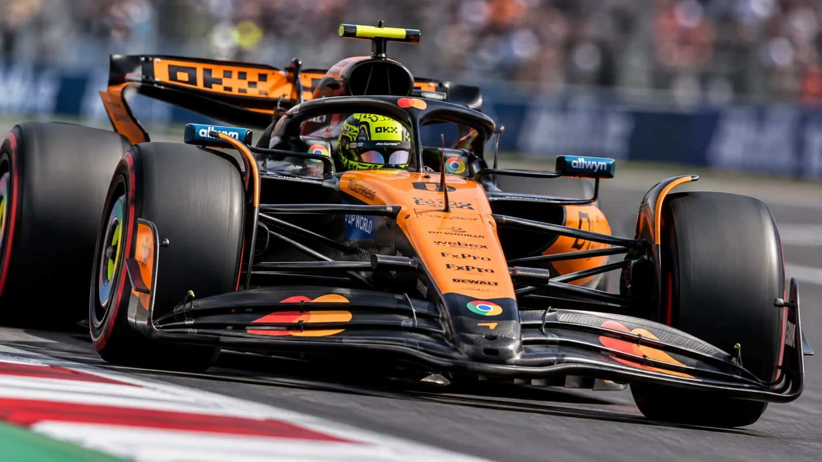 Narancssárga Formula–1-es versenyautó nagy sebességgel halad a versenypályán.